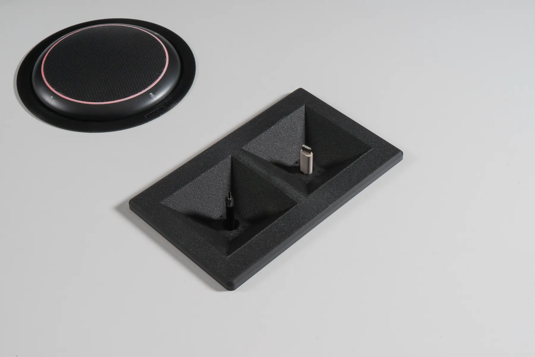 Close-up of a charcoal Kubby Dos rectangle with cables, next to a conference speakerphone